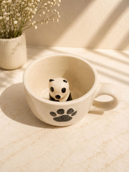 Ceramic cup with a panda design on a light surface, next to a small plant.