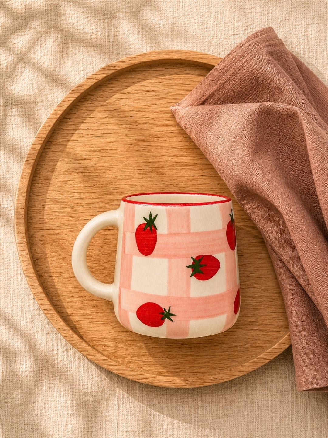Pink mug with red tomato pattern on a wooden tray with a pink cloth