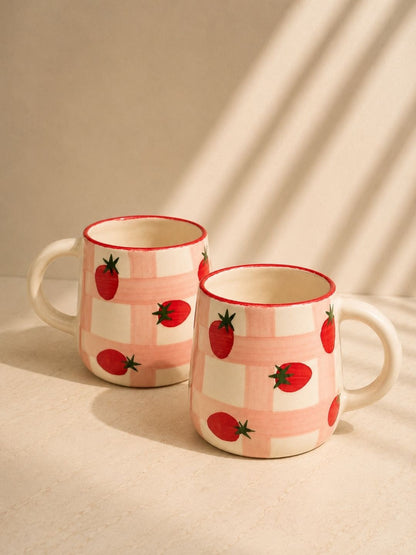 Two ceramic mugs with strawberry pattern on a beige background
