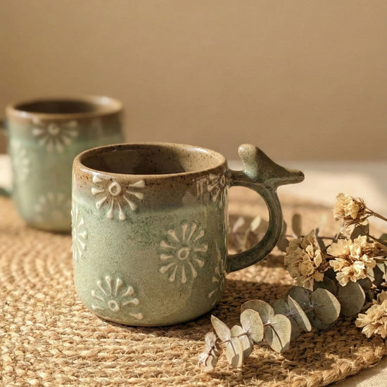Macro video pans across the surface of a seafoam green stoneware mug, showing the tactile raised daisy details and the artistic imperfections of the handcrafted reactive glaze.