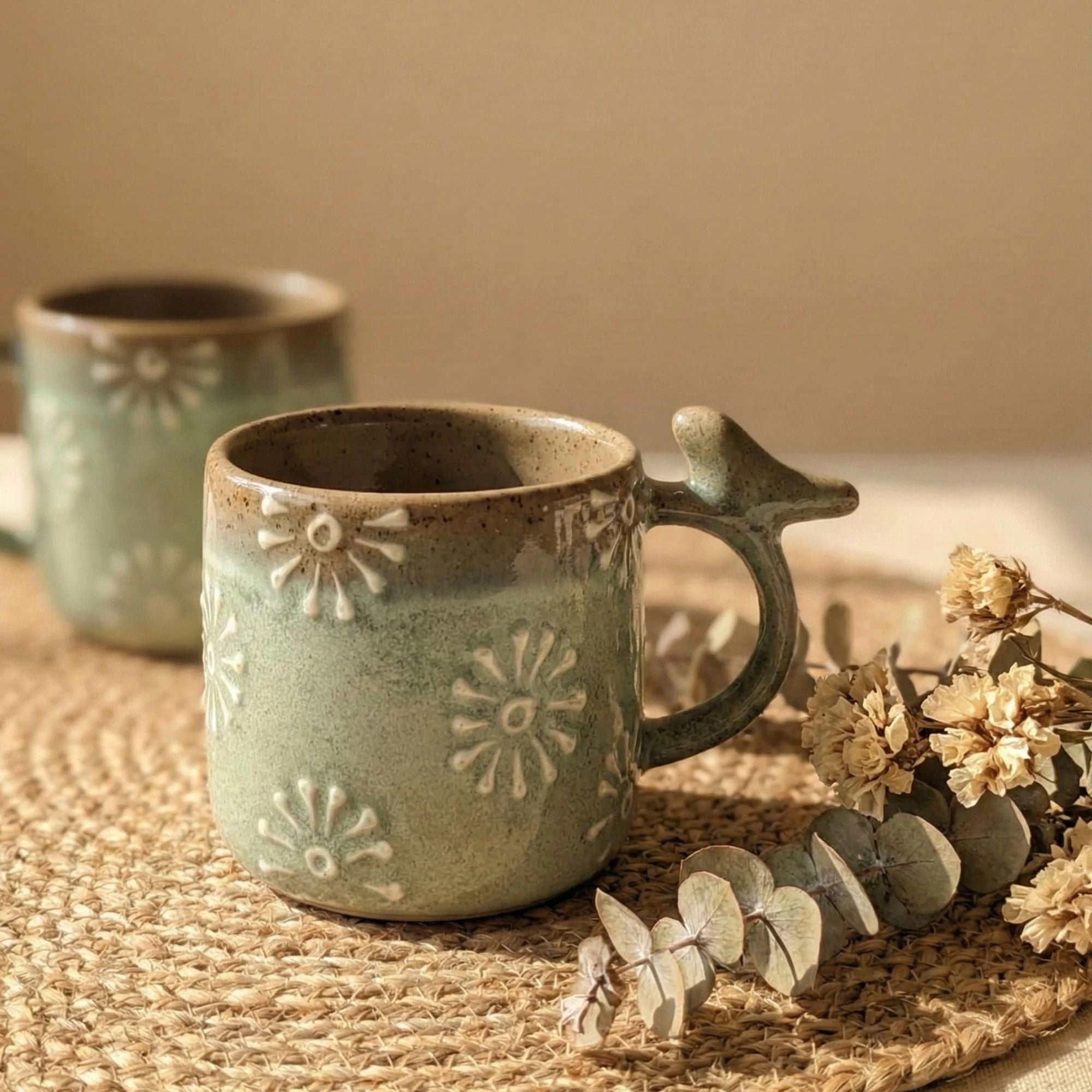 Macro video pans across the surface of a seafoam green stoneware mug, showing the tactile raised daisy details and the artistic imperfections of the handcrafted reactive glaze.